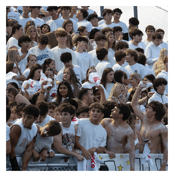 A large group of people wearing mostly white shirts are gathered closely together in bleachers, some holding white towels and two shirtless individuals with painted bodies are raising their fists. Description generated by AI