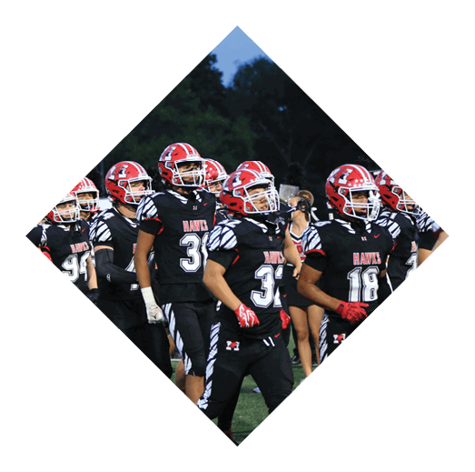 A group of people wearing black football uniforms with red helmets and the word “HAWKS" on their jerseys are walking together on a grassy field. Description generated by AI