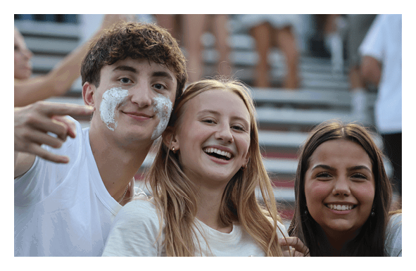 Two people smiling and posing closely together, one wearing a white shirt with some white substance on their face. Description generated by AI