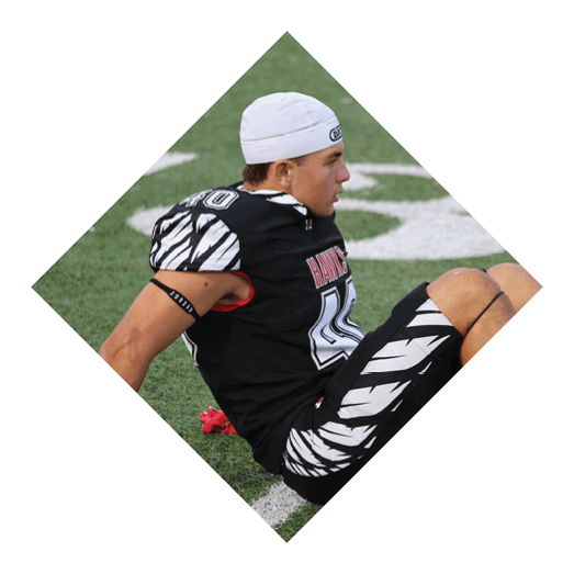 A person wearing a black sports uniform with white patterns and a white headband is sitting on a grassy field with knees bent. Description generated by AI