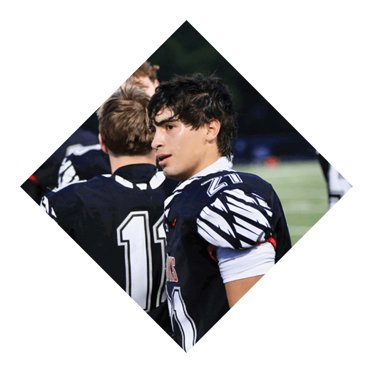 A person wearing a black and white sports jersey with the number 21 is standing next to another person in a black jersey with the number 11 on a sports field. Description generated by AI