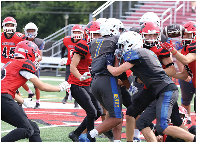 Several people wearing football helmets and uniforms are engaged in a close play on a football field with one person holding the ball. Description generated by AI
