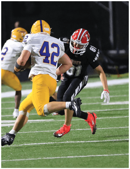 Two people in football uniforms are actively engaged in a play on a field, with one wearing yellow pants and a white jersey running while the other in a black uniform attempts to block or tackle. Description generated by AI