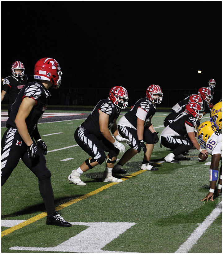 Two opposing American football teams in black and white and yellow and white uniforms are lined up facing each other on a field at night. Description generated by AI
