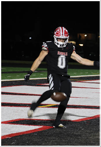 A person wearing a black football uniform with the number zero is kicking a football on a field at night. Description generated by AI