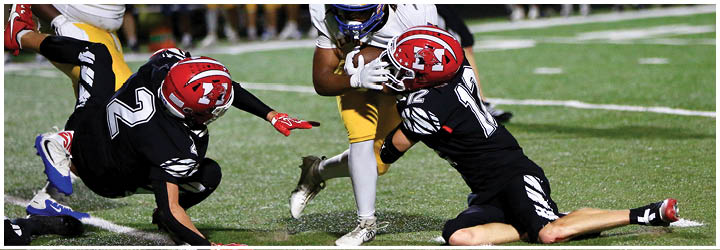 Two people in black sports uniforms are diving on a grassy field near a person in yellow pants and white shoes. Description generated by AI