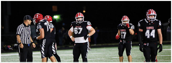 Five people in football uniforms and one referee in a striped shirt are standing on a field at night. Description generated by AI