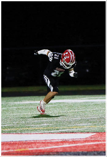 Two people in football uniforms are running on a field near a 20-yard marker at night. Description generated by AI
