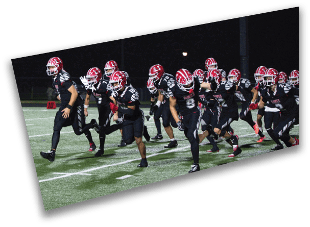 People wearing football uniforms and helmets are lined up on a field at night, preparing for a play. Description generated by AI