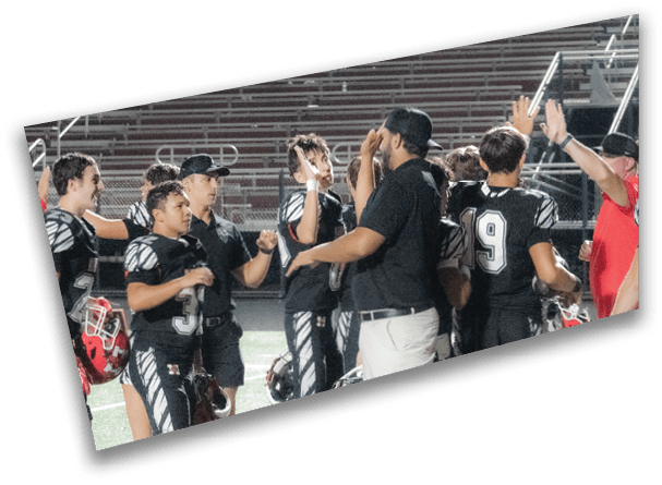 People in sports uniforms and casual clothing are gathered on a field, some raising their hands in celebration or greeting. Description generated by AI