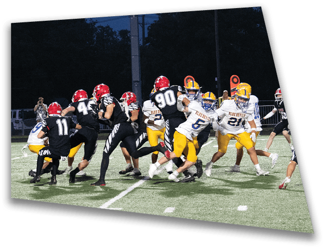 A group of people wearing football uniforms in black and red helmets are playing against a team in yellow pants and white jerseys on a lit outdoor field at night. Description generated by AI