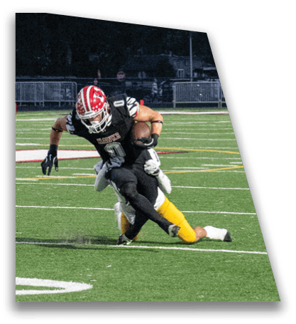 A person wearing a black sports uniform is running with a football while another person in a white and yellow uniform attempts to tackle them on a green football field. Description generated by AI