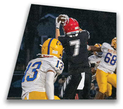 Several people in football uniforms are actively engaged in a play on a field during a game at night. Description generated by AI