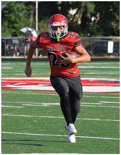 A person wearing a red football uniform with “Maine South" on the jersey is running on a football field while holding a football. Description generated by AI
