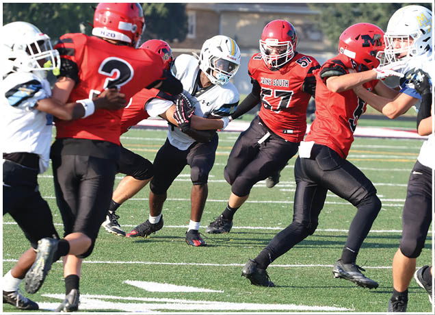 Several people wearing football uniforms are engaged in a play on a grassy field with some players attempting to block or tackle others. Description generated by AI