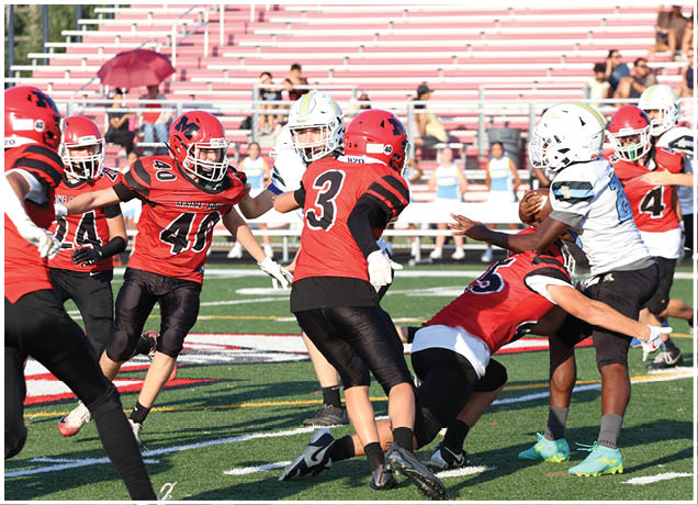 Several people wearing football helmets and uniforms are actively engaged in a play on a football field with empty bleachers in the background. Description generated by AI