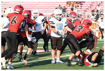 People in football uniforms are actively engaged in a game on a field with bleachers and spectators in the background. Description generated by AI