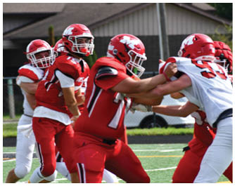 Several people wearing red football helmets and uniforms are gathered outdoors near a utility pole and a house. Description generated by AI