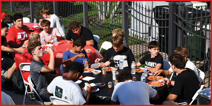 A group of people sitting around a table outdoors eating a meal together with plates of food and bottles of water. Description generated by AI