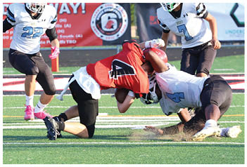 Two people in white football uniforms with helmets are running on a field while a person in a red and white uniform is on the ground during a game. Description generated by AI