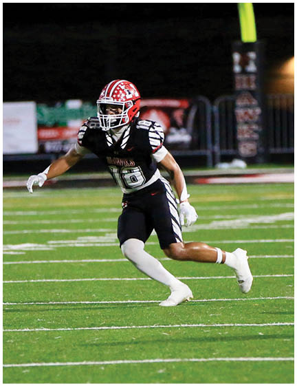A person wearing a red helmet and black football uniform is running on a green football field at night. Description generated by AI
