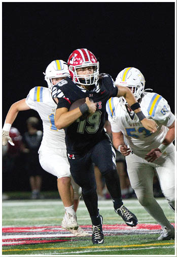 Two people in black sports uniforms with red helmets are running on a football field while a person in a white uniform is chasing them. Description generated by AI