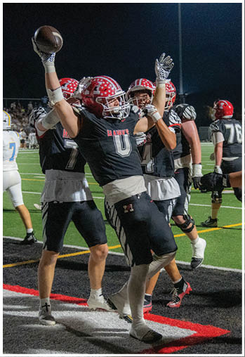 People wearing black football uniforms with red helmets celebrate on a field under stadium lights at night. Description generated by AI