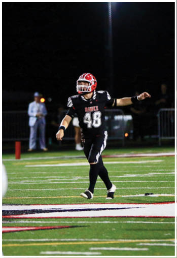 Two people in football uniforms are on a field at night, with one person in white preparing to move and another in black pointing while standing near the goal line. Description generated by AI