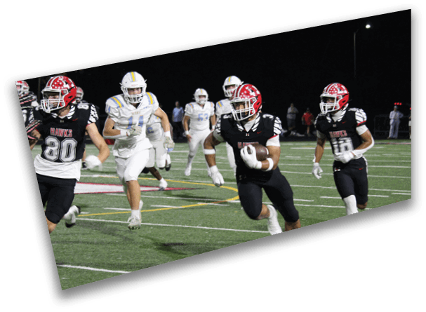 Two people wearing black and white football uniforms are running on a green field with white yard lines. Description generated by AI