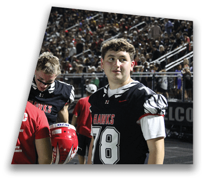 Two people wearing black sports jerseys with “HAWKS" written on them are standing in a crowded outdoor setting. Description generated by AI