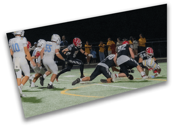 People wearing football uniforms are actively playing on a field under stadium lights at night. Description generated by AI