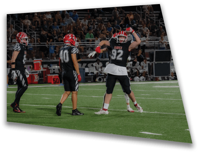 Two people in football uniforms stand on a field with one raising their arms and the other facing them. Description generated by AI