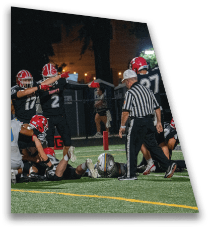 Several people in football uniforms are gathered on a field at night with some lying on the ground near a referee. Description generated by AI