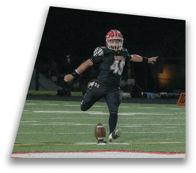 A person in a football uniform is kicking a football on a field at night. Description generated by AI