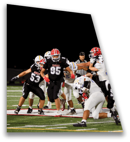 Players in black and white football uniforms are actively engaged in a play on a well-lit field during a nighttime game. Description generated by AI