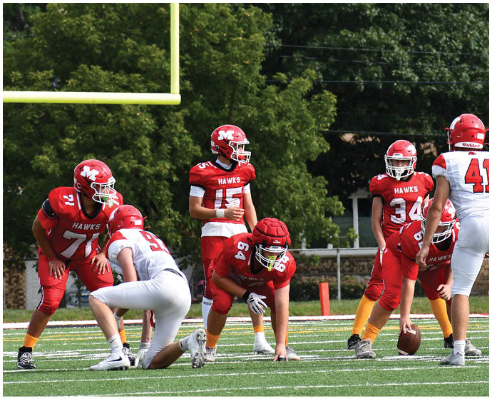 Several people in red and white football uniforms are positioned on a grassy field near a goalpost, appearing to prepare for a play. Description generated by AI