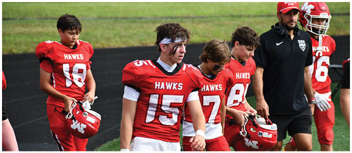 People wearing red football uniforms and holding helmets are walking on a field. Description generated by AI