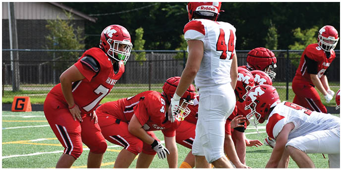 Adults in red and white football uniforms are lined up on a green field preparing for a play. Description generated by AI