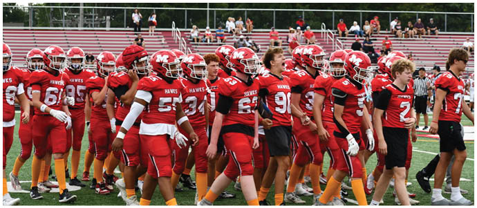A group of people wearing red football uniforms with orange socks are walking together on a green field. Description generated by AI