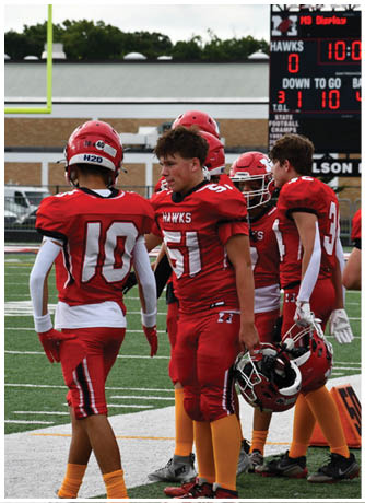Adults wearing red football uniforms and orange socks stand on a field holding red helmets. Description generated by AI