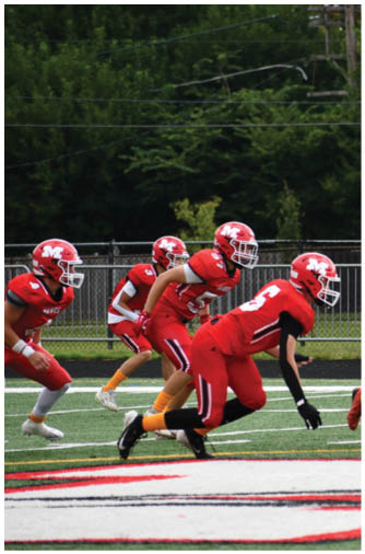 Three people in red football uniforms and helmets are in a ready stance on a football field with a green turf and white yard lines. Description generated by AI