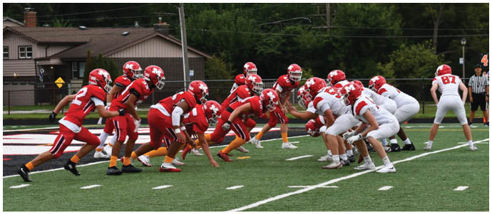 Two teams of people in football uniforms are lined up facing each other on a field, preparing for a play. Description generated by AI