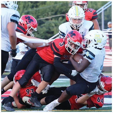 Two people in white football uniforms and two people in red football uniforms are engaged in a tackle during a game on a field. Description generated by AI