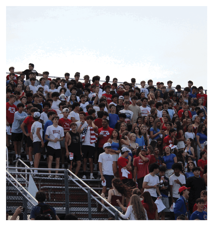 A large group of people wearing casual clothing and some in sports-themed attire are gathered closely together on bleachers, appearing engaged and attentive. Description generated by AI