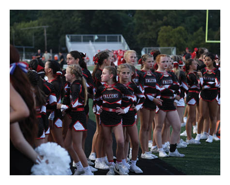 A group of people wearing black and red cheerleading uniforms with the word Falcons stand together on a sports field. Description generated by AI