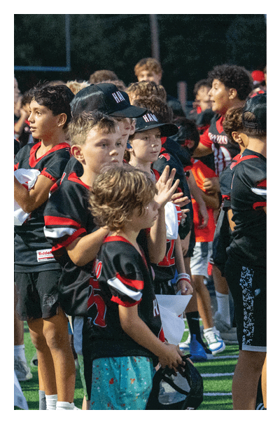 Children wearing sports uniforms and caps are standing closely together, appearing focused and attentive. Description generated by AI