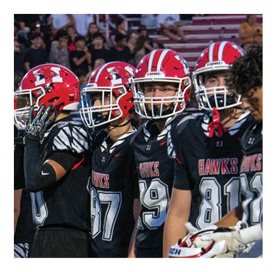 A group of football players in black uniforms with red helmets stand together on the field with one player holding a football and wearing a white cap labeled “SOUTH." Description generated by AI