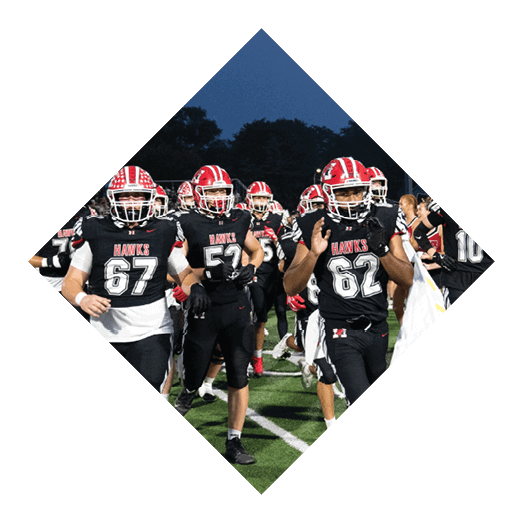 A group of people wearing black sports uniforms with red and white helmets are running on a football field under a darkening sky. Description generated by AI