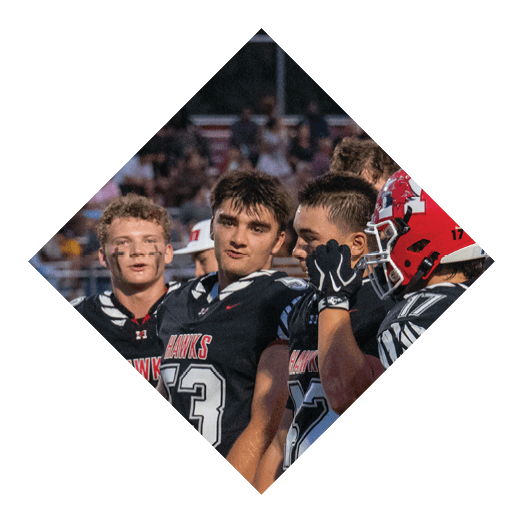 A group of people wearing black football uniforms with red helmets are standing together on a field with a crowd in the background. Description generated by AI