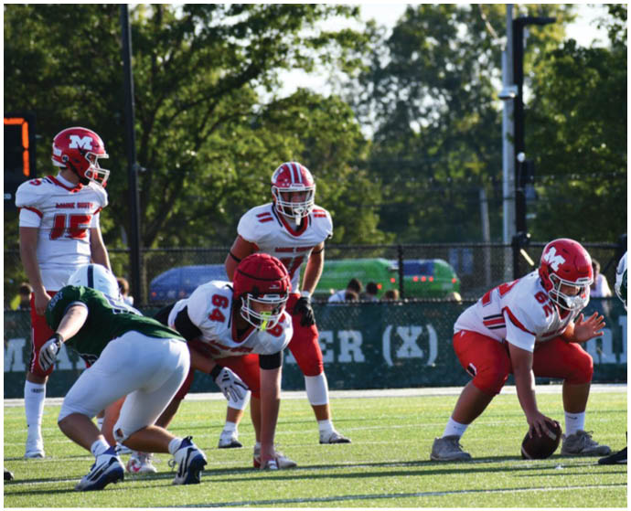 People in football uniforms are positioned on a field preparing for a play during a game. Description generated by AI